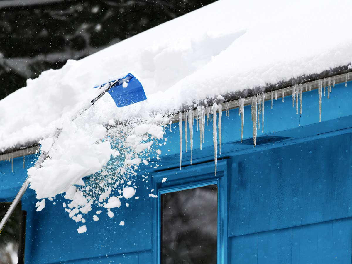 Accumulation de neige et de glace sur le toit et la gouttière d’une maison bleue.