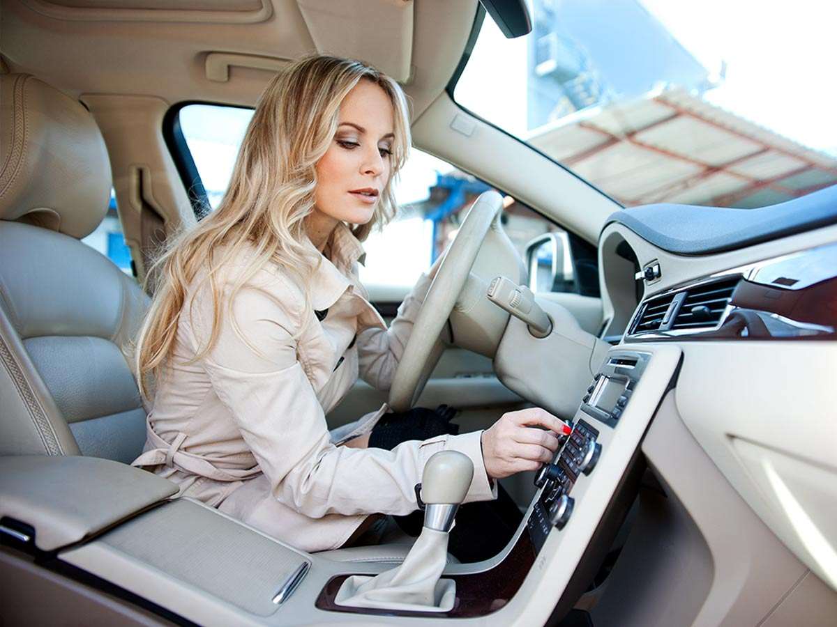 Une femme au volant d'une voiture ajuste le volume de son système de son.