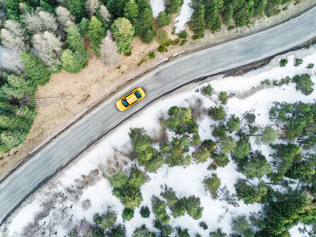 Une auto jaune sur la route en situation de conduite hivernale dans une zone boisée.